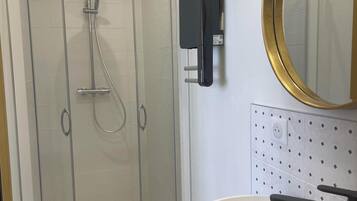 Un baño moderno con ducha de vidrio, lavamanos con tocador de madera y espejo montado en la pared.