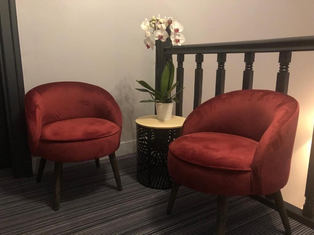 Two red chairs, a small round table with a plant, and a black railing.