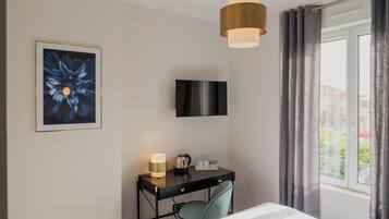 Habitación de hotel con una cama, un escritorio con lámpara, un televisor y una ventana con cortinas.