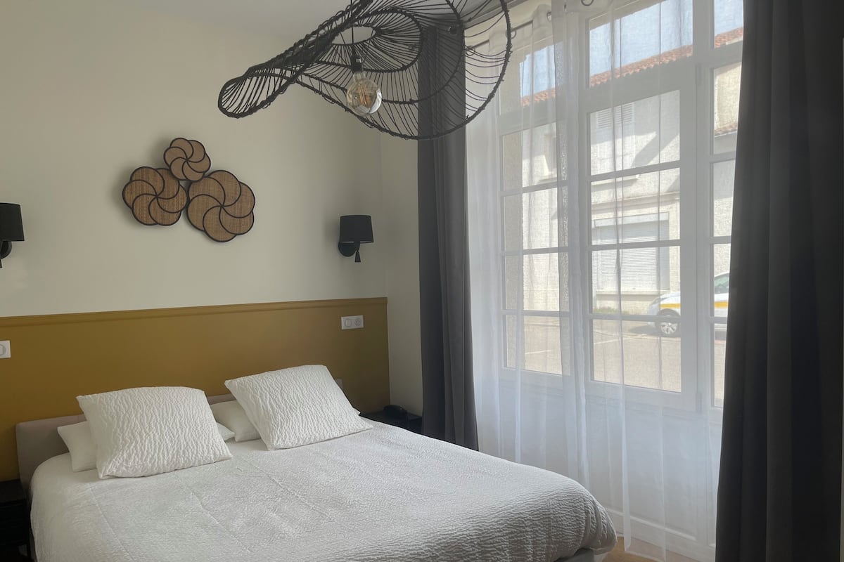 Habitación de hotel con una cama grande, una lámpara de pared y vistas al exterior a través de una ventana.