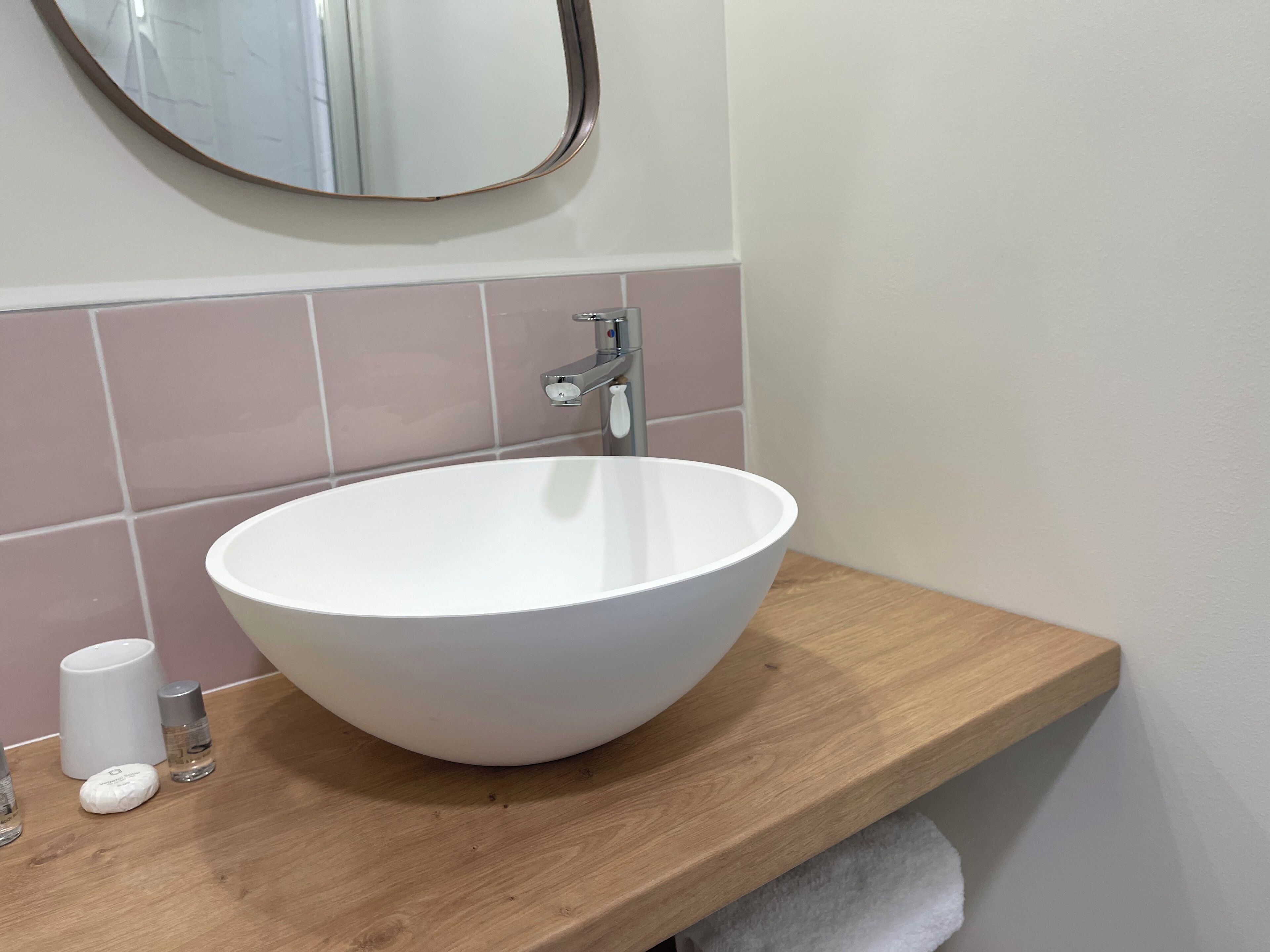 A bathroom with a white sink, a wooden countertop, a mirror, and pink tiles.
