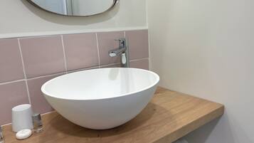 A bathroom with a white sink, a wooden countertop, a mirror, and pink tiles.