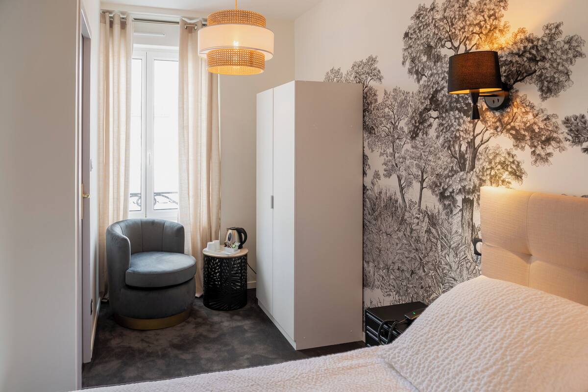 Un dormitorio con cama, una silla, un armario, una lámpara y un mural en la pared.