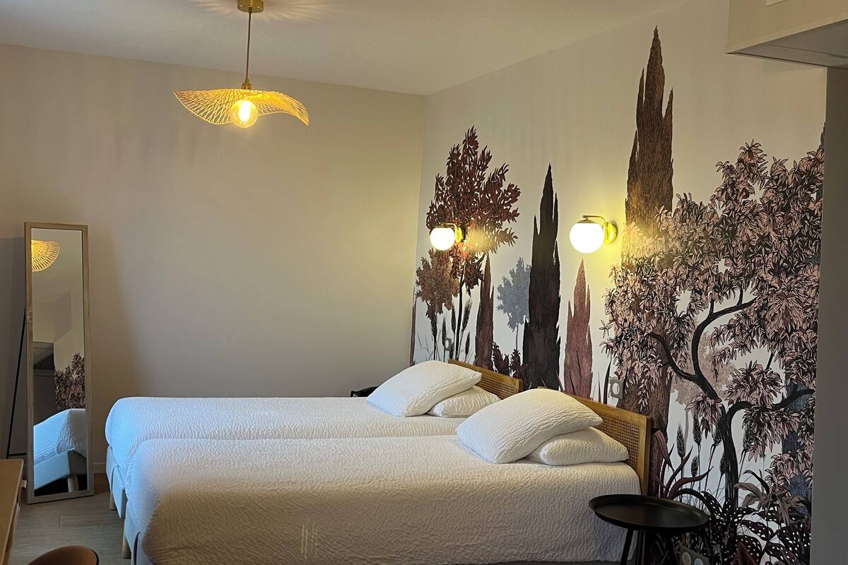 Una habitación de hotel con una cama grande, dos mesitas de noche, un espejo y un mural en la pared.