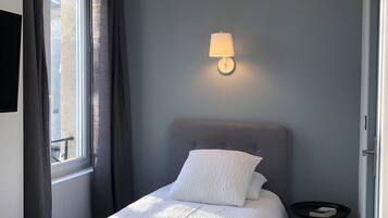 Ein ordentlich bezogenes Bett mit weißer Decke und Kissen, eine Wandlampe und eine besondere Deckenleuchte.