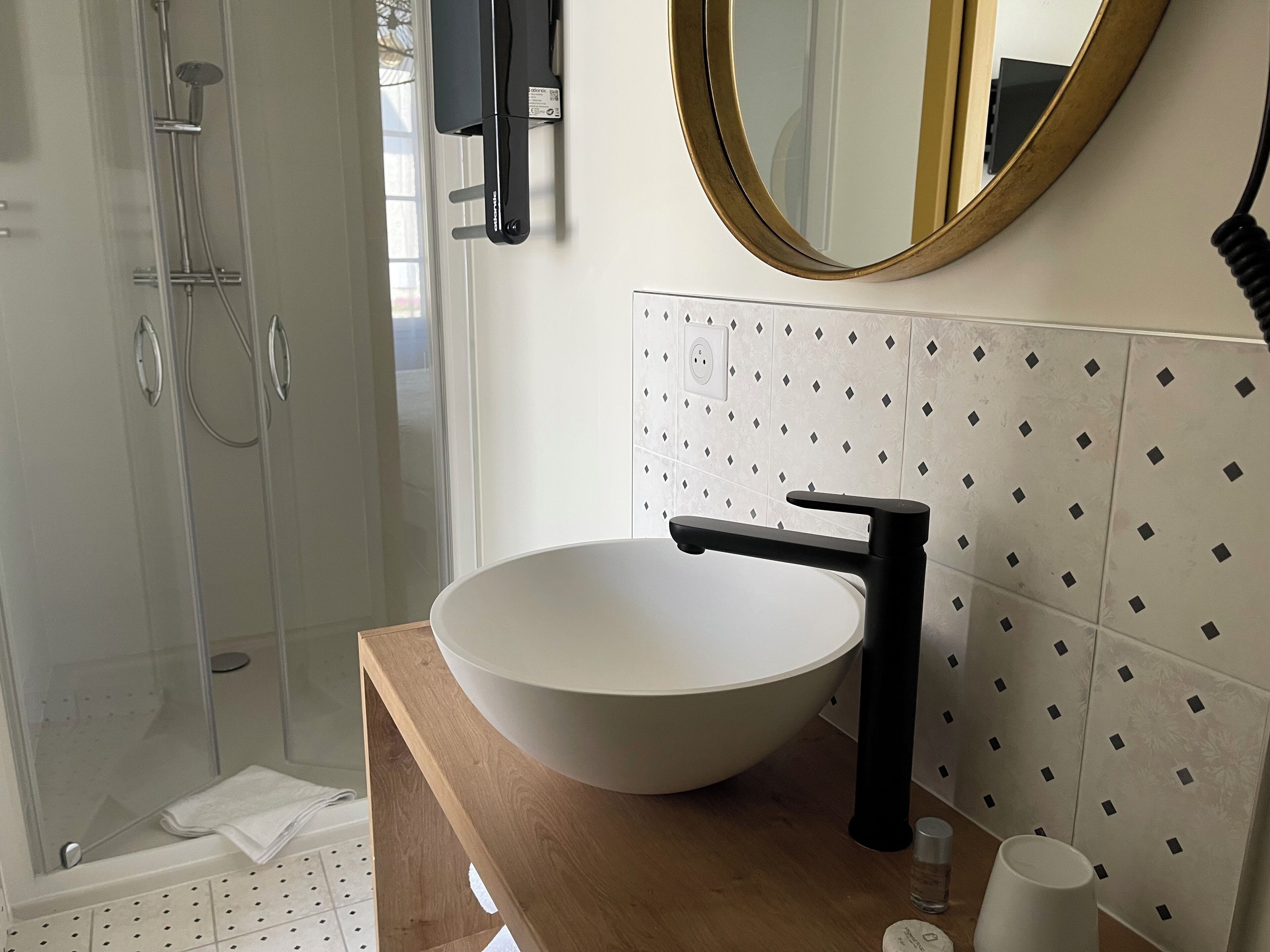 A modern bathroom with a large white sink, black faucet, and a round mirror with a gold frame.