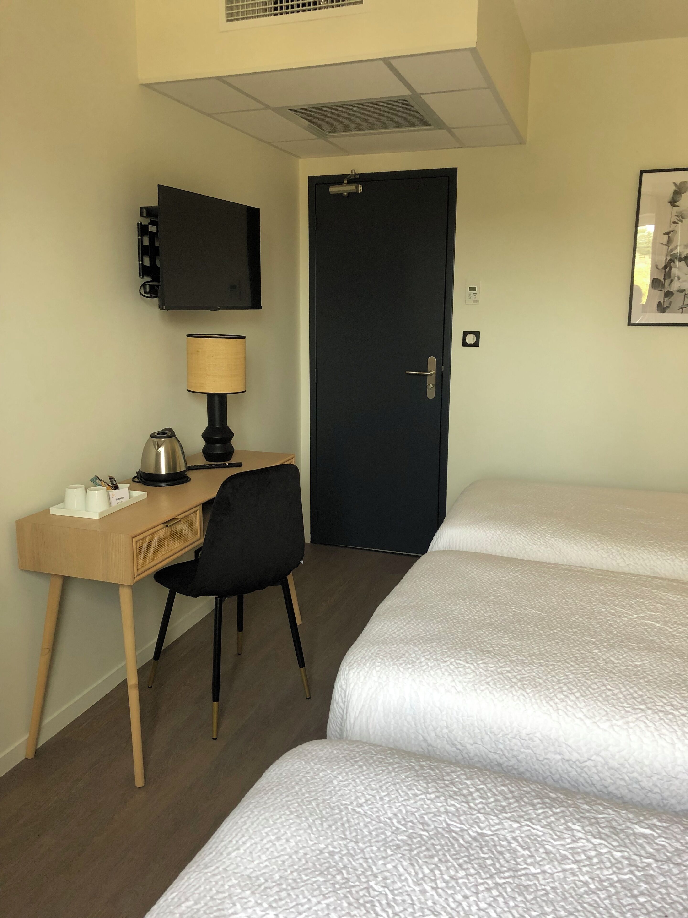 A hotel room with two beds, a desk with a lamp, a chair, a television, and a door.