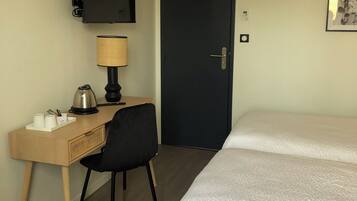 A hotel room with two beds, a desk with a lamp, a chair, a television, and a door.
