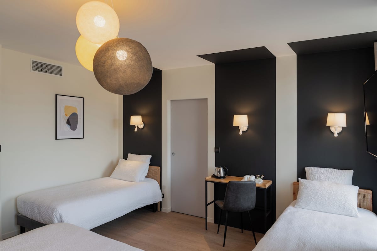 Una habitación de hotel moderna con dos camas individuales, un escritorio pequeño con una silla y una lámpara fijada a la pared.