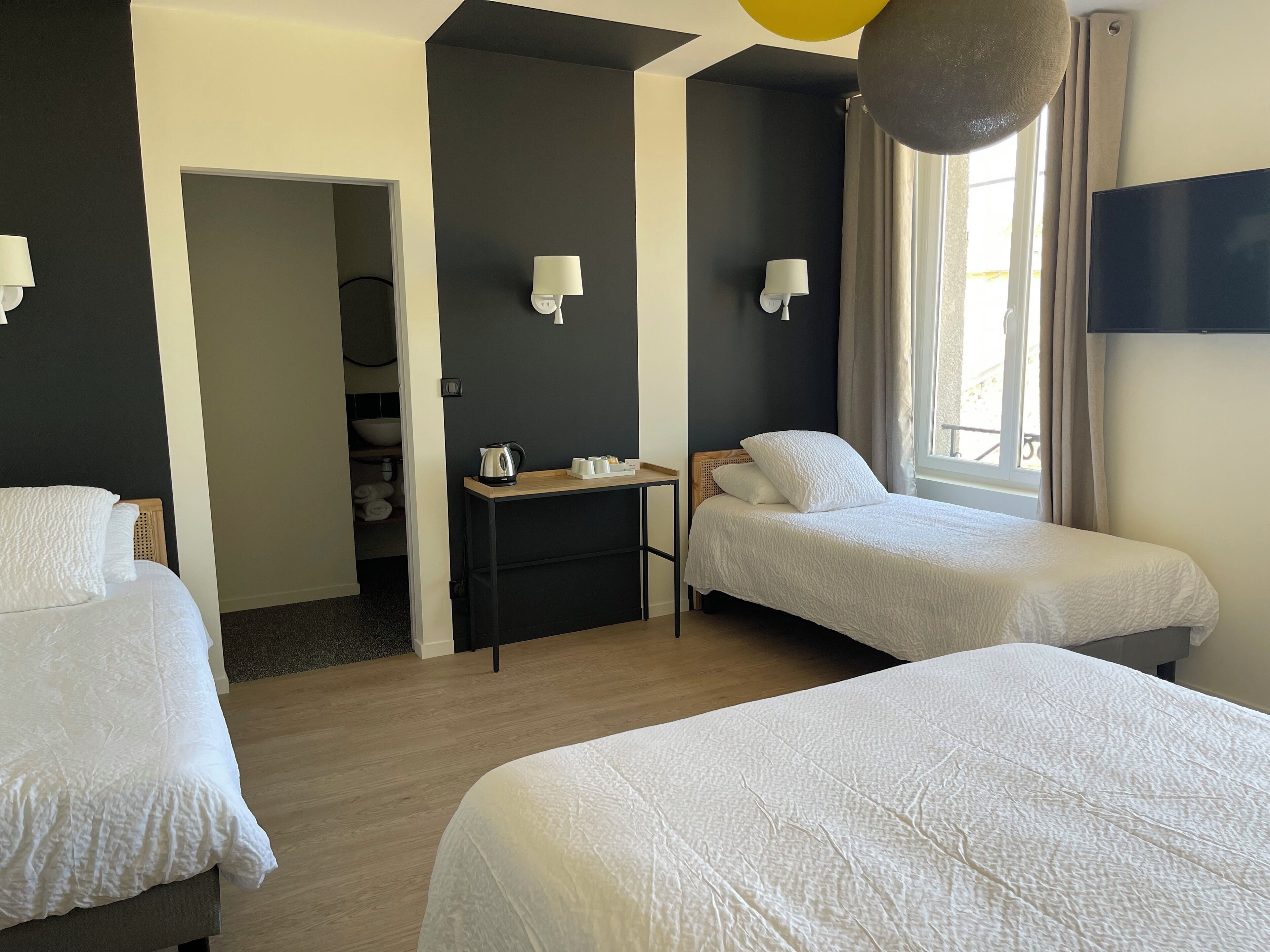 Habitación de hotel con dos camas individuales, una mesita con hervidor, televisión y ventana con cortinas.