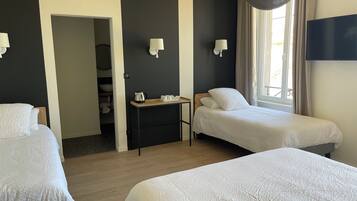 Habitación de hotel con dos camas individuales, una mesita con hervidor, televisión y ventana con cortinas.
