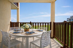 A round table set for four with white chairs, a wicker basket with flowers, and a view of a grassy area and buildings in the background. - Apartment for 4–6 people with port view, Port Bourgenay (Talmont-Saint-Hilaire)