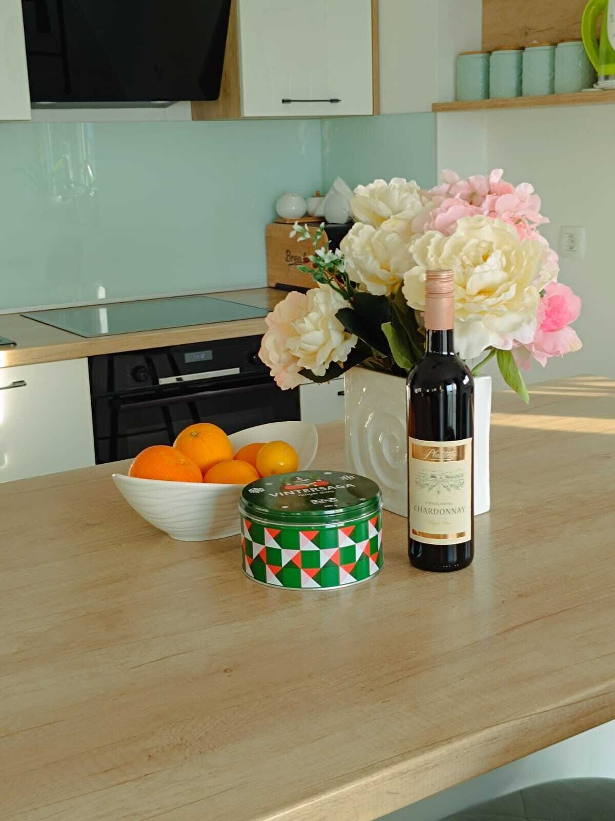 A kitchen counter with a bottle of wine, a bowl of oranges, and a decorative tin.
