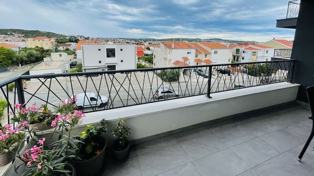 Un balcón con vistas a una zona residencial, plantas en macetas y baranda de metal.
