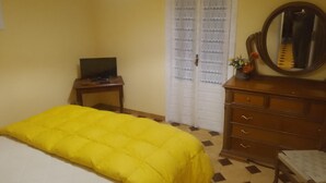 Een kamer met een bed, een dressoir, een spiegel, een televisie en een deur met kantgordijnen.