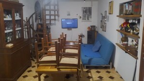 Een woonkamer met een houten eettafel, stoelen, een blauwe bank, een televisie en een trap.