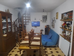 Ein Wohnzimmer mit einem Holzespeise Tisch, Stühlen, einem blauen Sofa, einem Fernseher und einer Treppe.