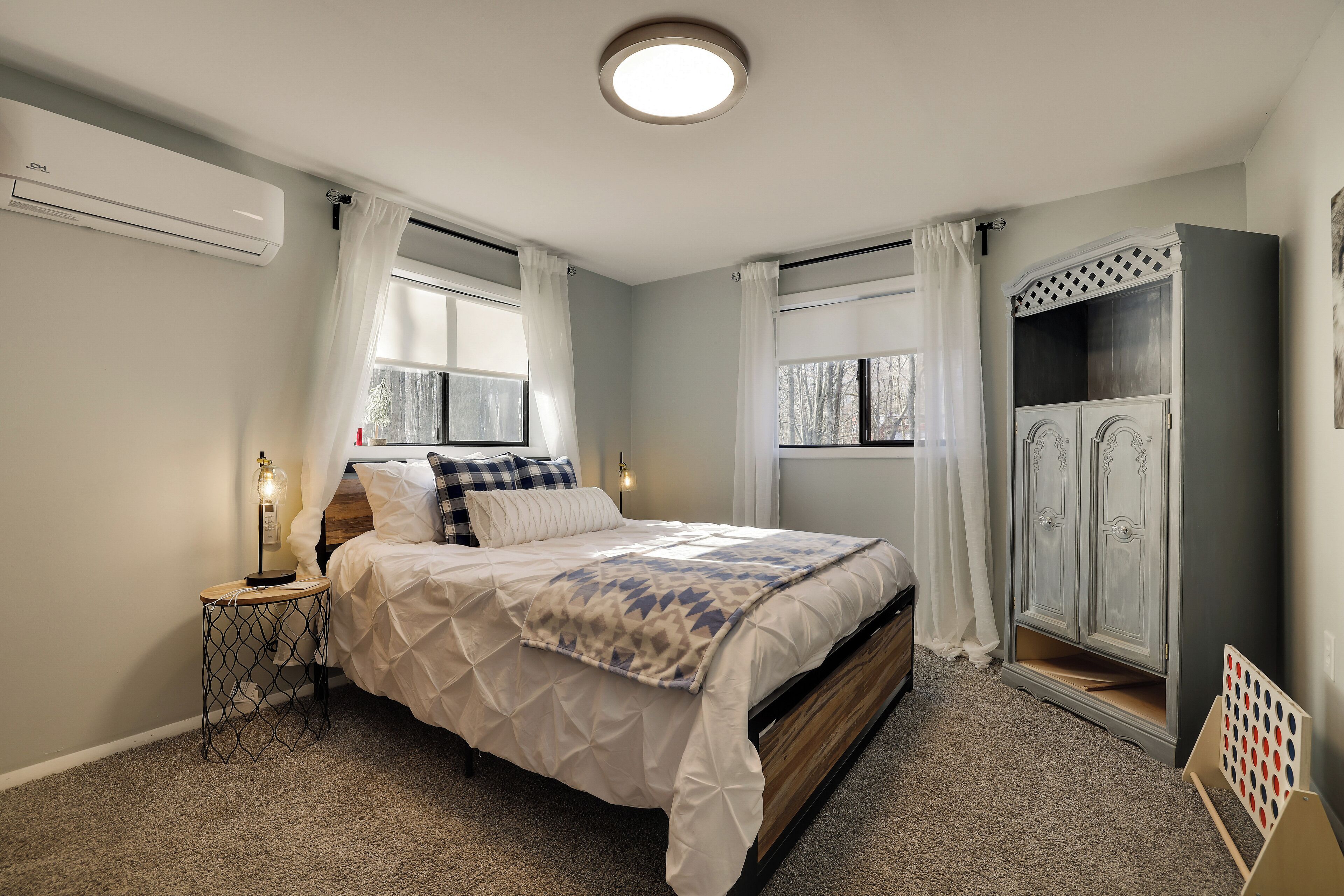 Un dormitorio con cama, mesita de noche, aire acondicionado, armario y ventana con cortinas.