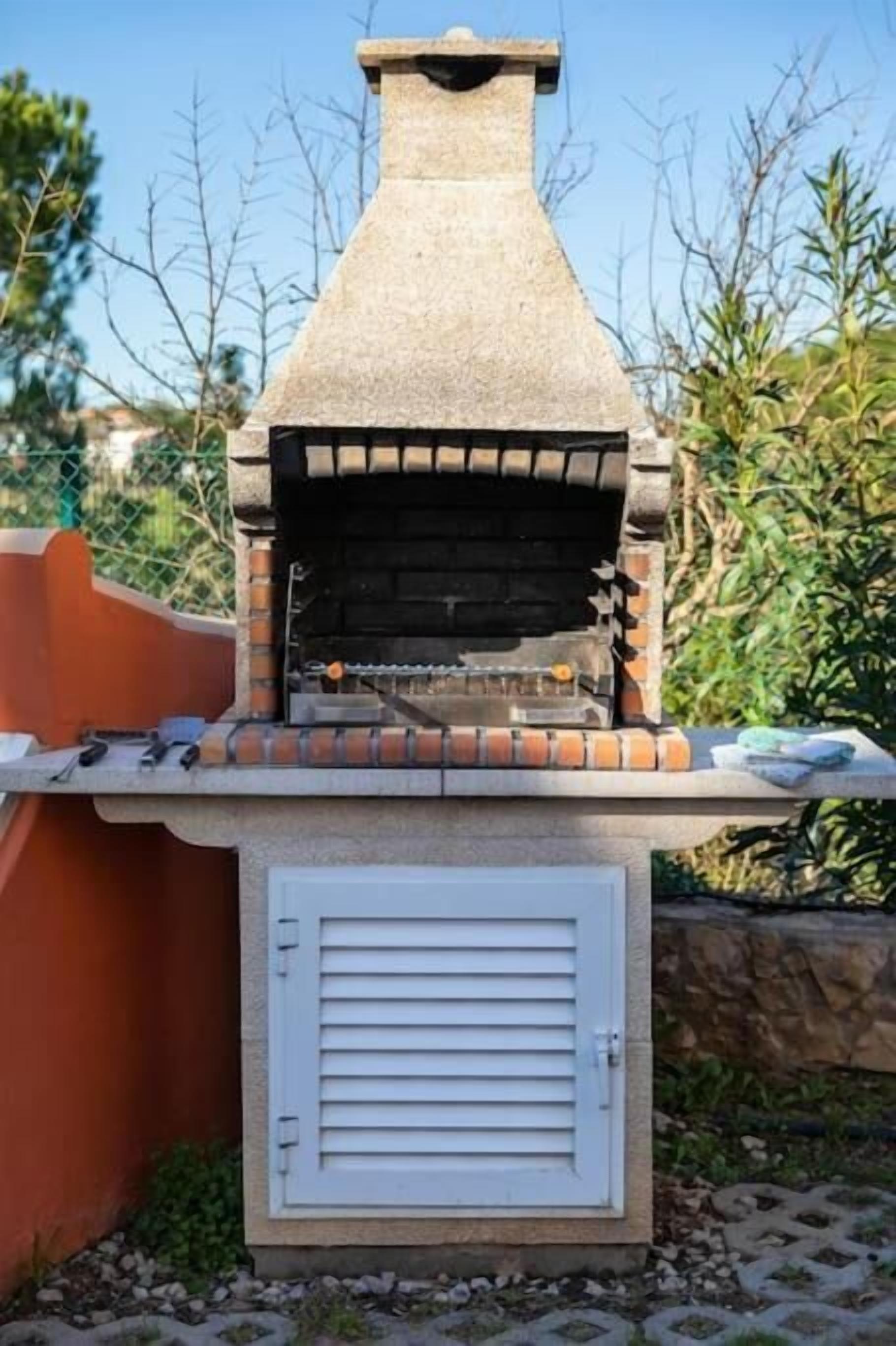 An outdoor brick oven with a chimney, a white door, and a small countertop with tools.