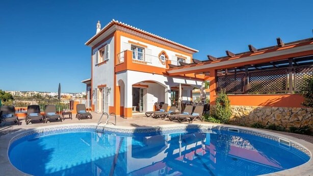 A two-story building with a swimming pool, lounge chairs, and a pergola.