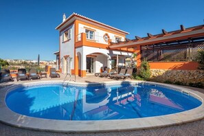 Un edificio de dos pisos con piscina, sillas de descanso y una pérgola.