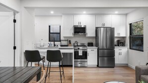 A modern kitchen with white cabinets, stainless steel appliances, and a wooden dining table with two chairs. - Pacific Beach Surf Nook Blocks to Surf & Sand (San Diego)