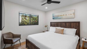 A bedroom with a bed, a chair, a nightstand, a ceiling fan, a window with a view, and a painting on the wall. - Pacific Beach Surf Nook Blocks to Surf & Sand (San Diego)