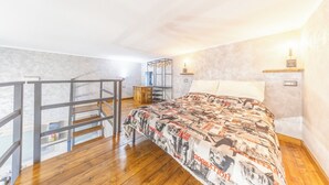 A bedroom with a bed, wooden flooring, a staircase, and a small desk area.