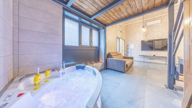 A modern bathroom with a large bathtub, a sofa, and a TV in the adjacent living area.