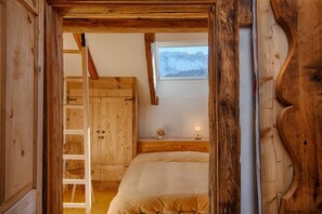 Ein Zimmer aus Holz mit einem Bett, einer Leiter und einem Fenster mit Blick auf die Berge.