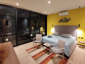 Ein modernes Schlafzimmer mit einem großen Bett, zwei Stühlen, einem kleinen Tisch und einer Glastür zum Balkon.