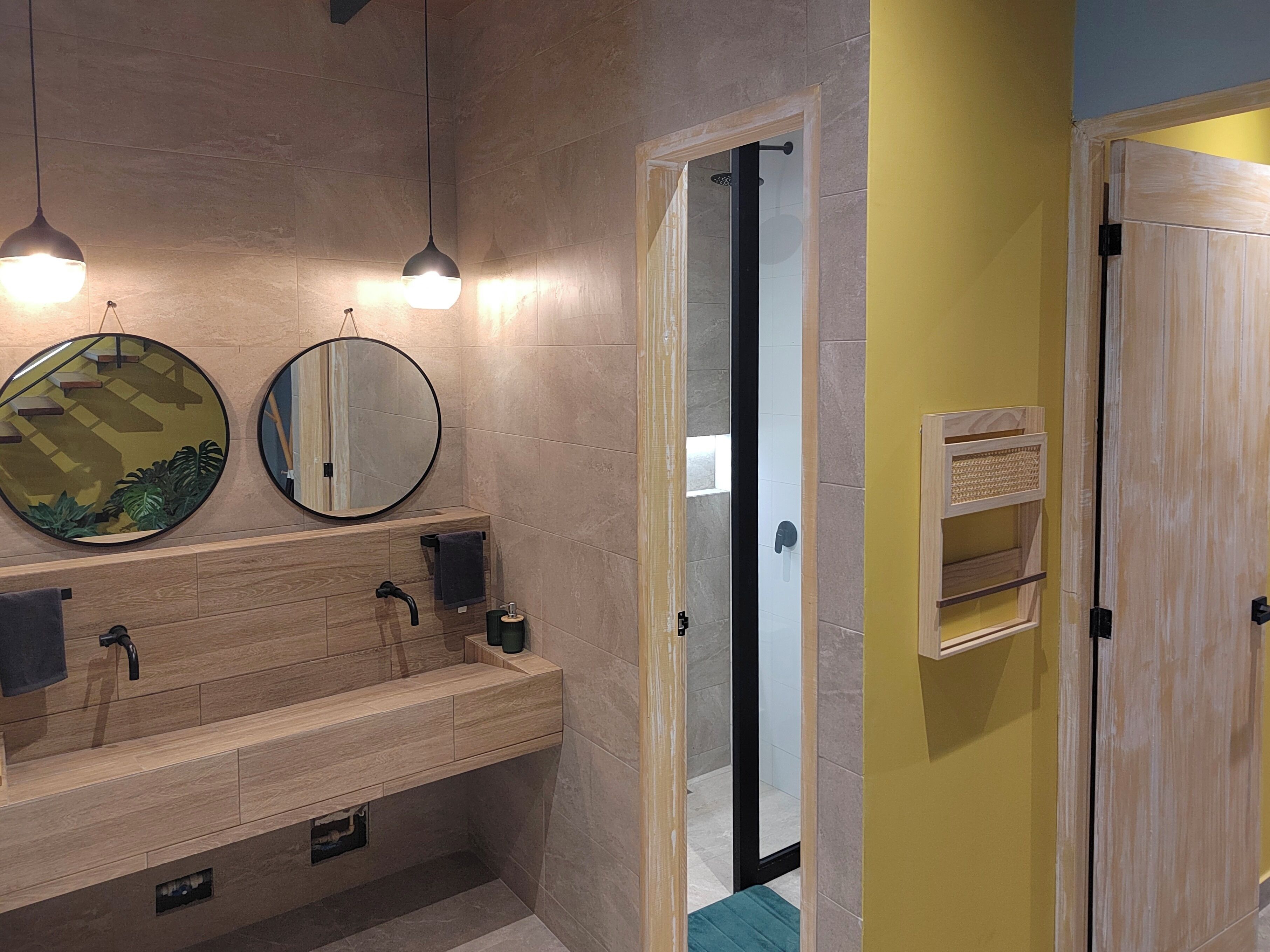 Un baño moderno con tocador de madera, dos espejos redondos y cabina de ducha con mampara de vidrio.