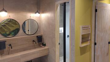 Un baño moderno con tocador de madera, dos espejos redondos y cabina de ducha con mampara de vidrio.