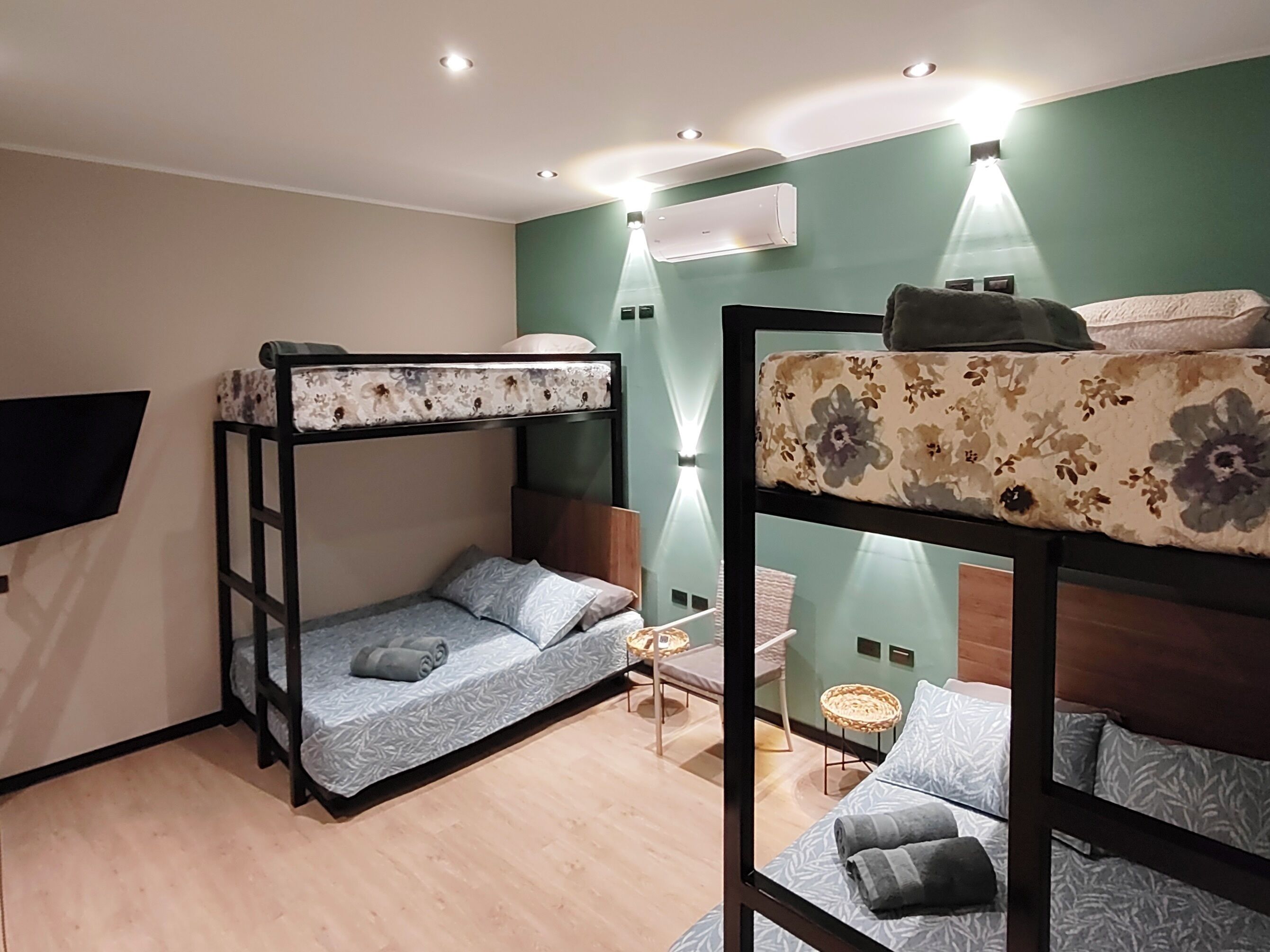 A dormitory room with bunk beds, a small table, and a wall-mounted air conditioner.