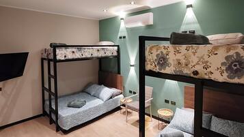 A dormitory room with bunk beds, a small table, and a wall-mounted air conditioner.