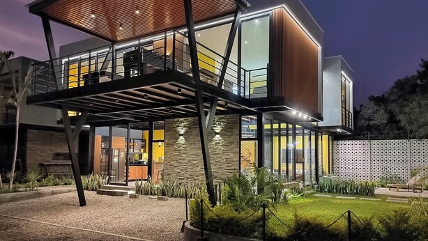 A modern two-story building with a glass facade, a wooden deck, and a stone wall.