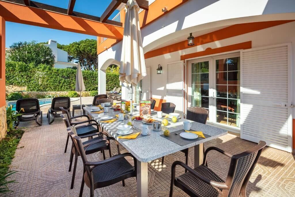An outdoor dining area with a table set for four, surrounded by chairs, and a pool in the background.