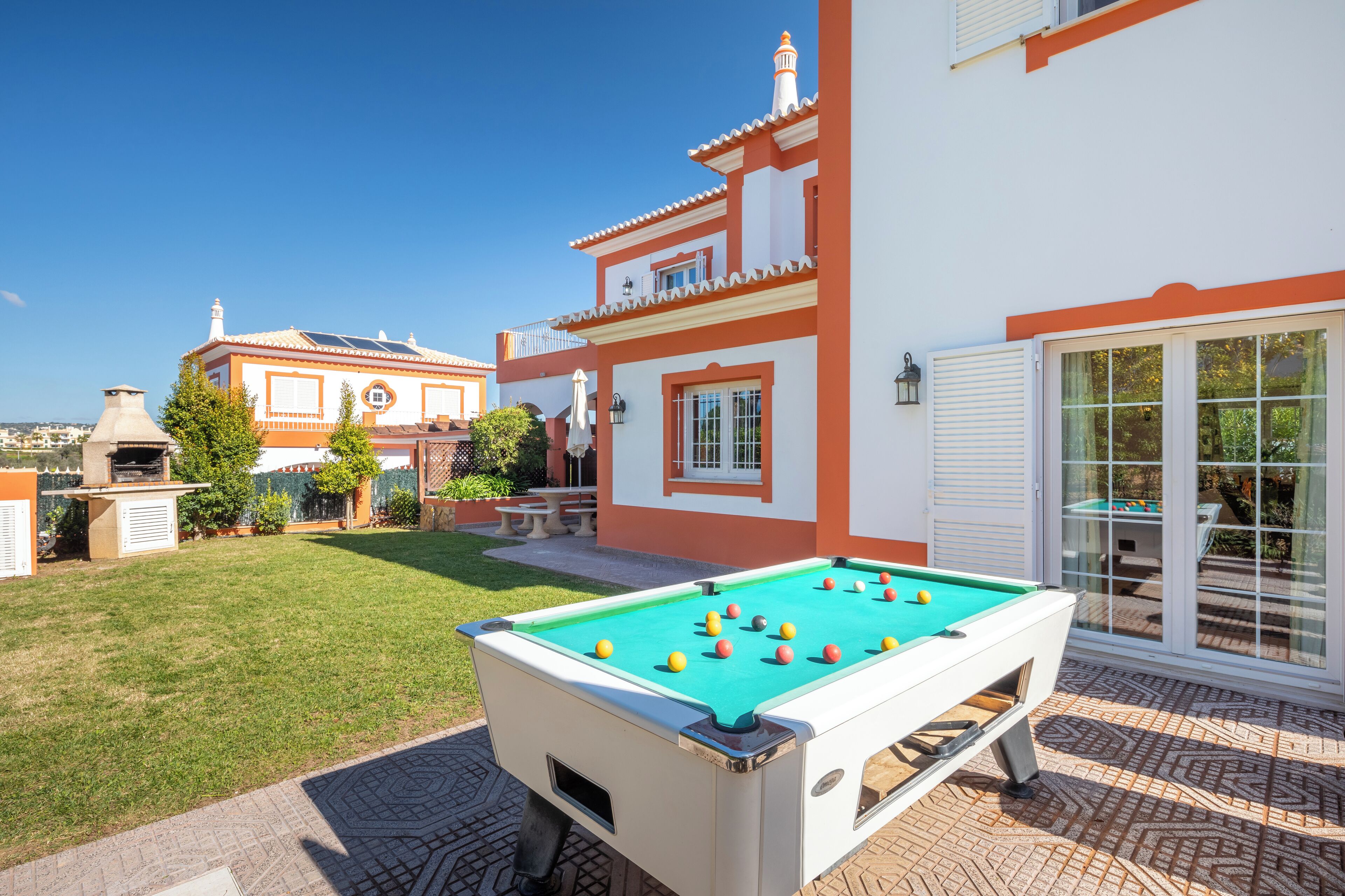 A pool table in a backyard with a patio area and a building with a tiled roof.