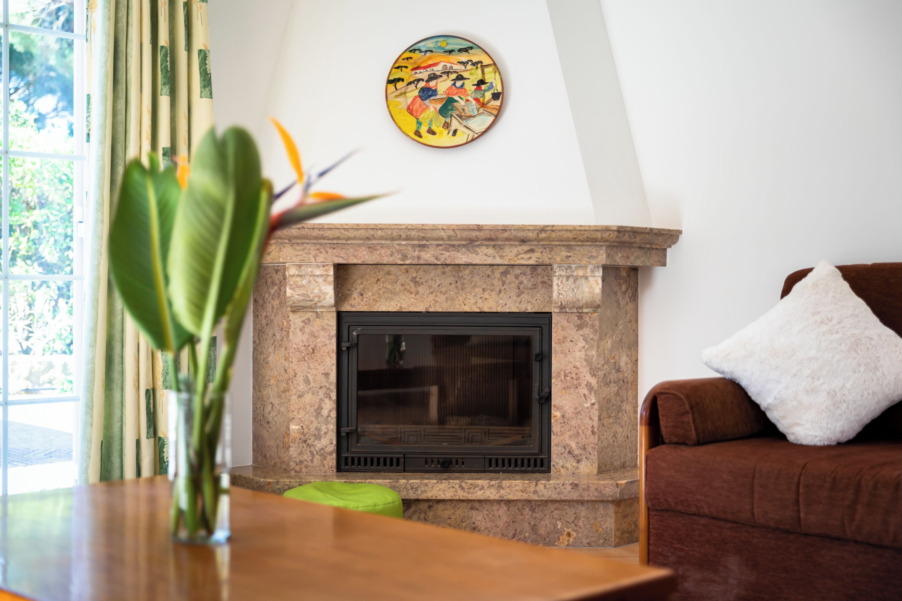 A living room with a fireplace, a couch, a green cushion, and a painting on the wall.