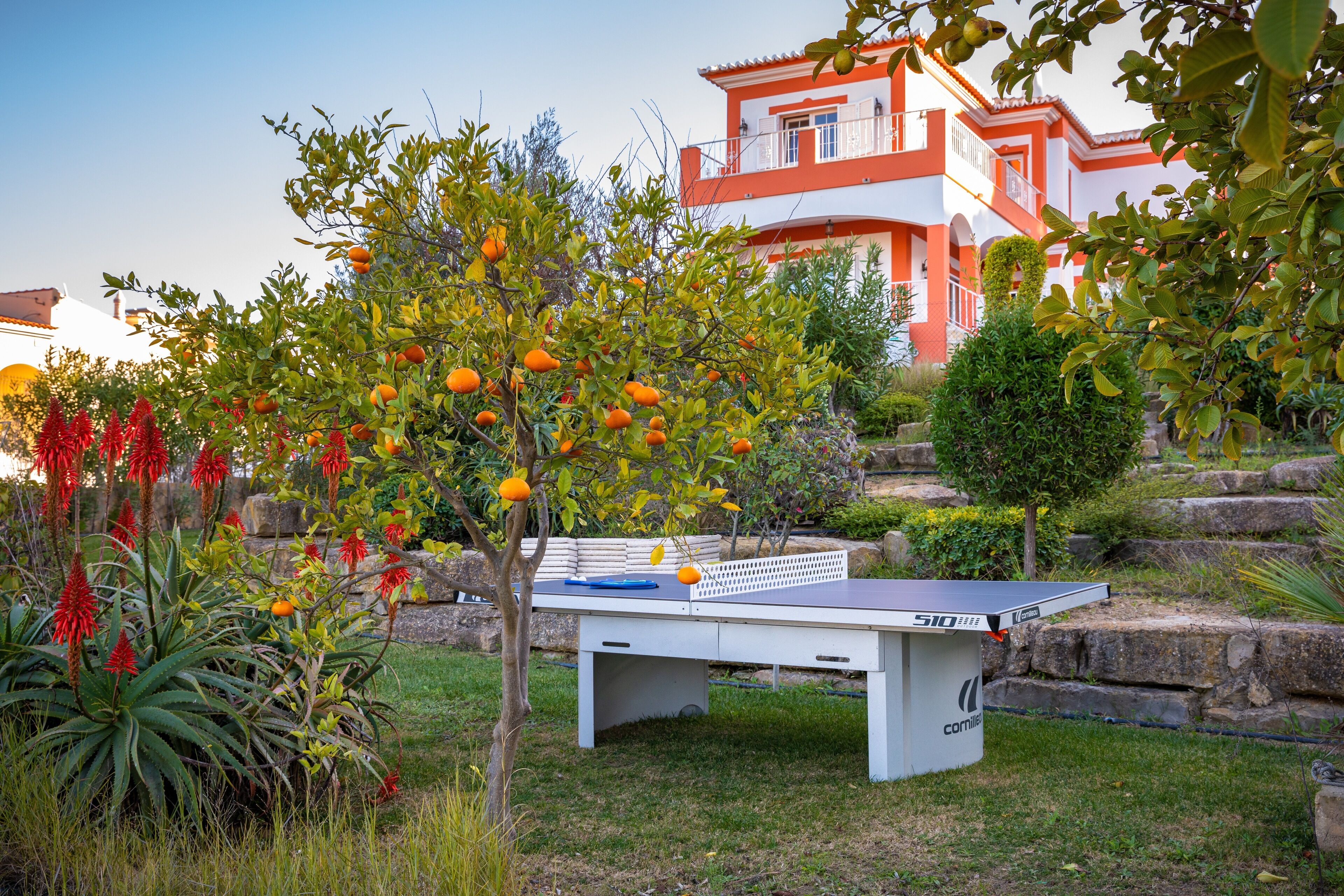 A ping pong table in a garden with a house in the background.
