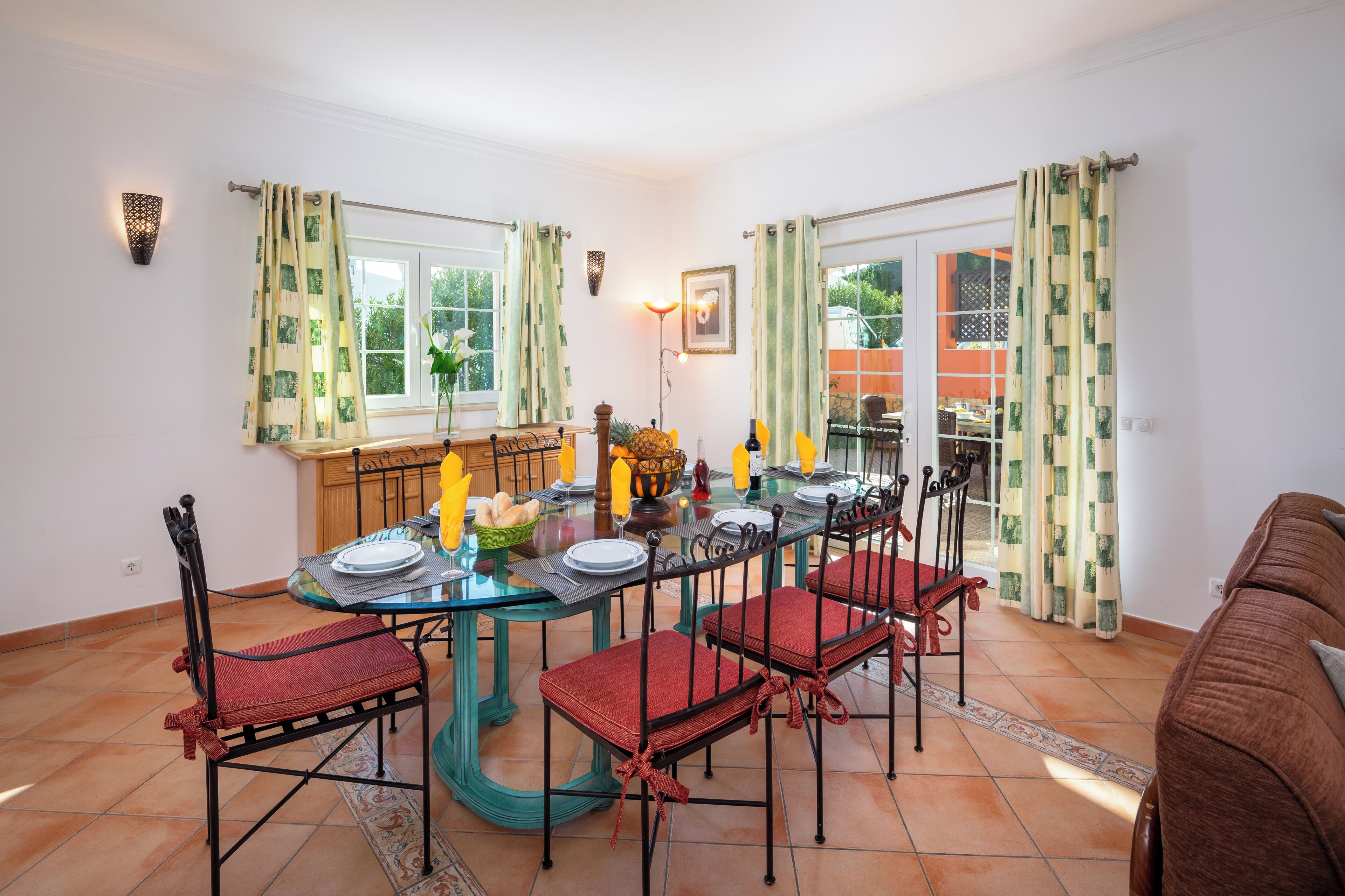Un comedor con una mesa de vidrio, sillas rojas y vistas al jardín a través de las ventanas.