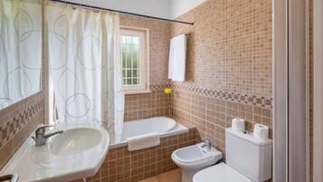 A bathroom with a sink, toilet, bidet, and a window with a curtain.