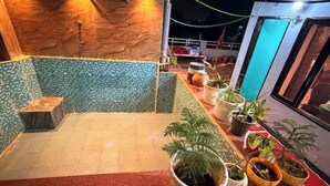 Une petite pièce agréable, avec un sol carrelé, un mur en bois et un banc recouvert de carreaux verts. Plusieurs plantes en pot sont disposées sur un comptoir.