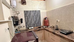 Eine kompakte Küche mit Marmorarbeitsplatte, einem Gasherd, einer Kaffeemaschine und einem kleinen Kühlschrank.