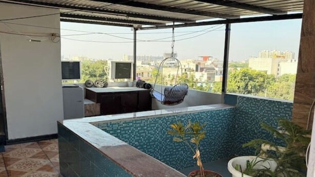 Ein Balkon mit Fliesenboden, einem Hängestuhl, einem kleinen Tisch mit Pflanze und Blick auf die Stadtlandschaft.