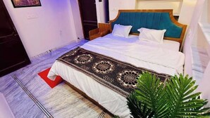 Ein ordentlich bezogenes Bett mit einem gemusterten Überwurf, einem hölzernen Kopfteil und einer kleinen Pflanze daneben.