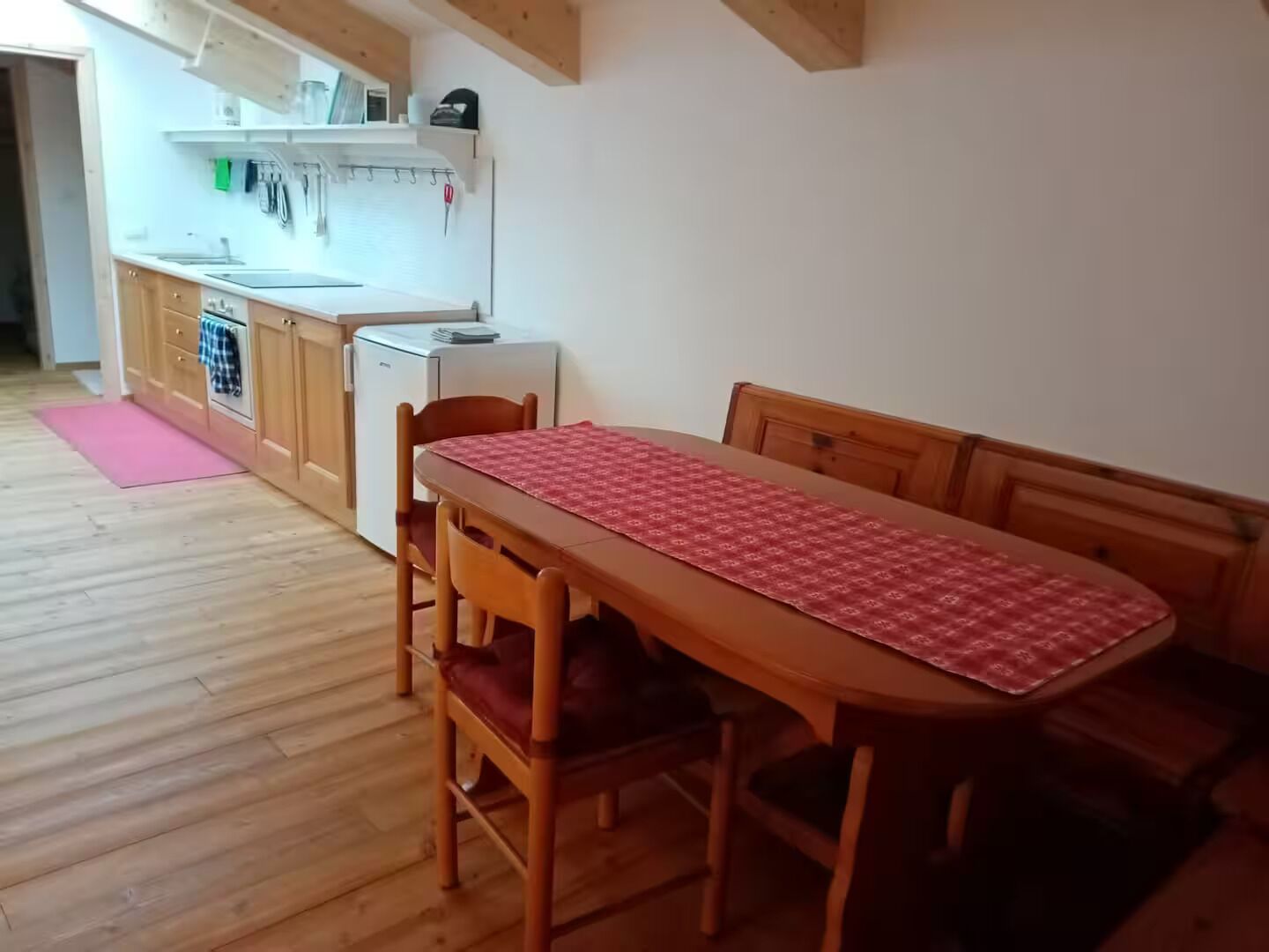 Eine kleine Küche mit Holzausstattung, einem Kühlschrank und einem Esstisch mit Stühlen.