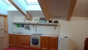 Eine Küche mit Holzausstattung, einem weißen Kühlschrank, einem kleinen Backofen und einem Oberlicht.