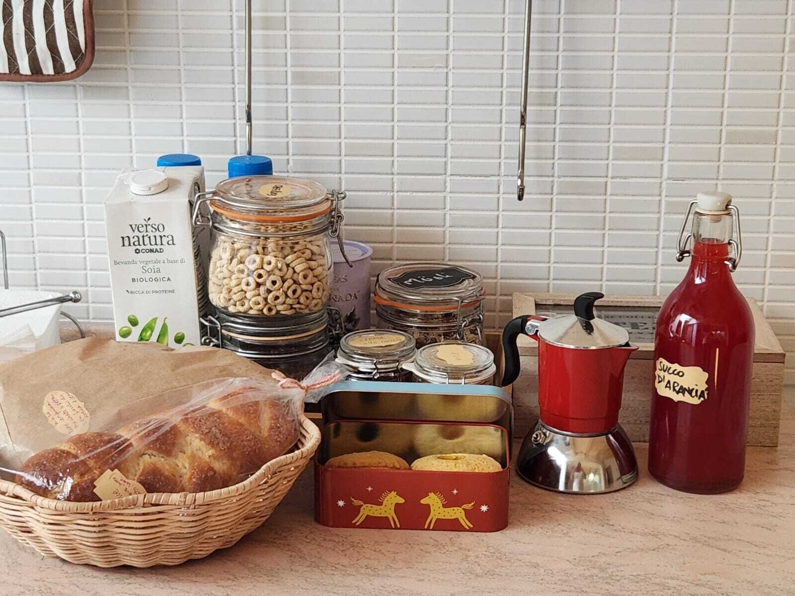 A kitchen counter with various food items and containers, including jars, a basket of bread, and a coffee pot.
