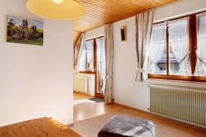 A room with a wooden ceiling, a radiator, a window with curtains, a door, and a painting on the wall.